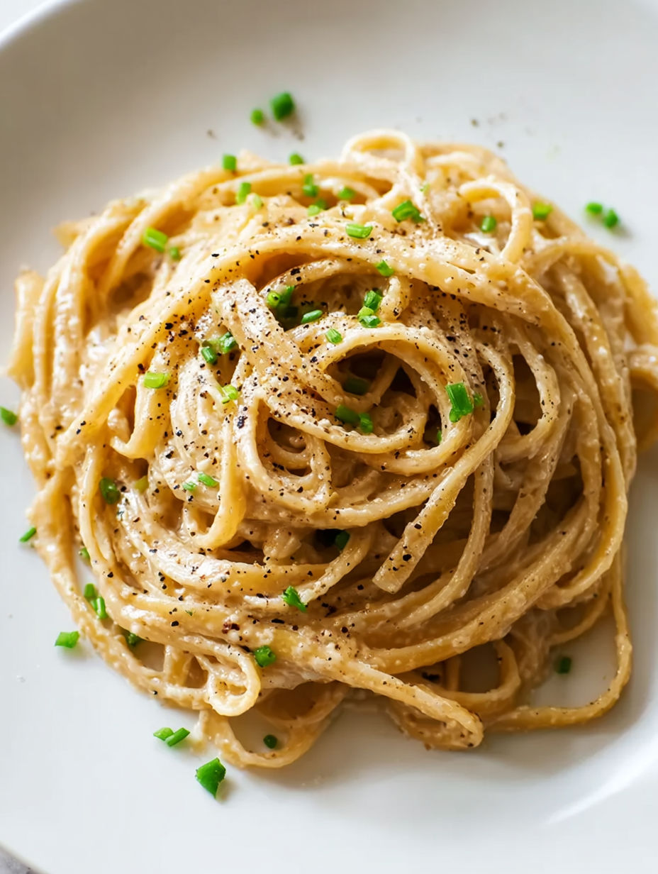 A plate of pasta with black pepper on top.
