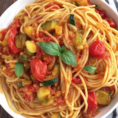 A bowl of pasta with tomatoes and zucchini.