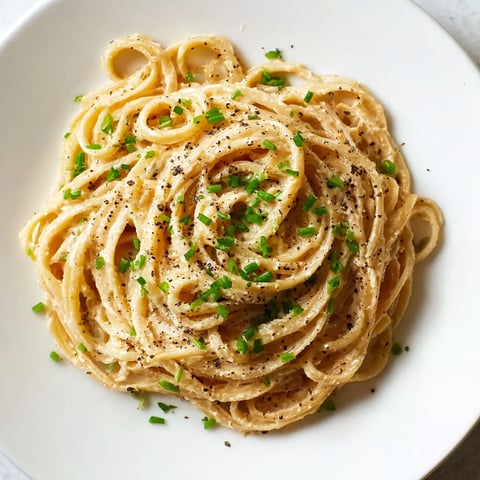 A plate of pasta with green onions on top.