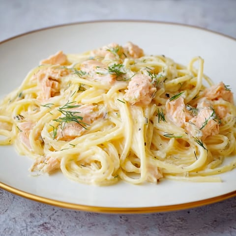 A plate of spaghetti with fish on top.